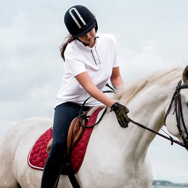 Young rider in white shirt on a white horse with red saddle pad